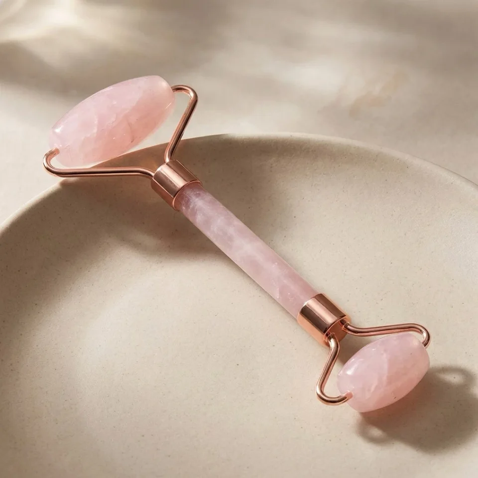 Beauty product image: rose quartz face roller on a beige ceramic dish