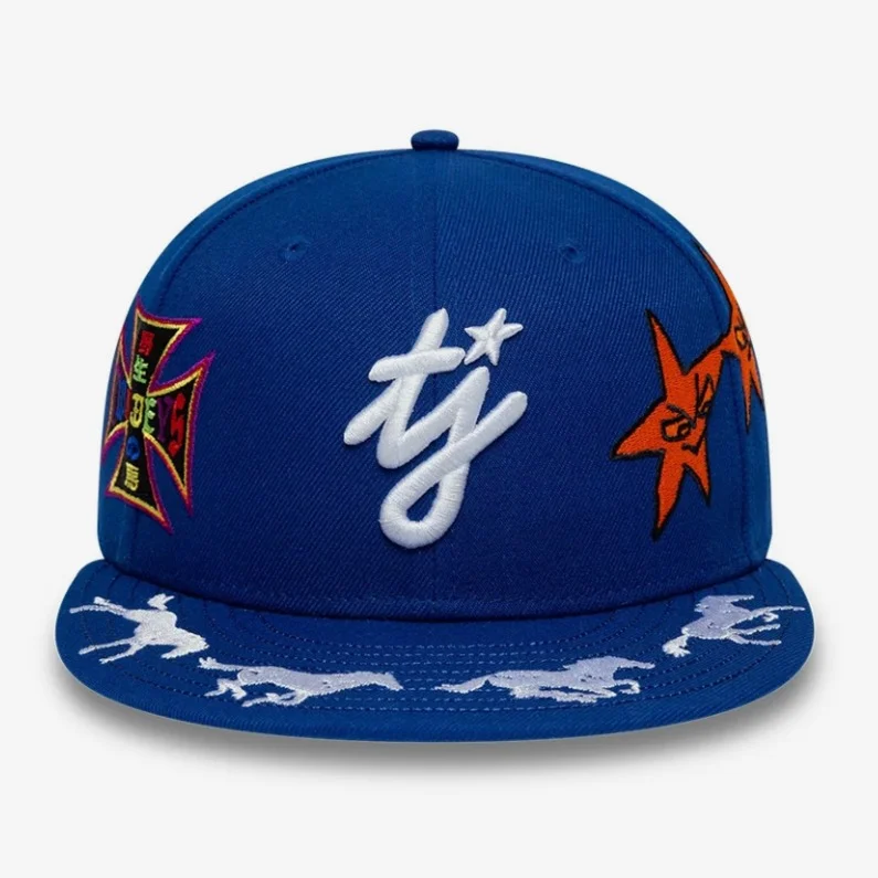 Original photo: blue fitted cap from the front, with an embroidered white script logo, a colorful cross patch, an orange star patch and white horses on the visor