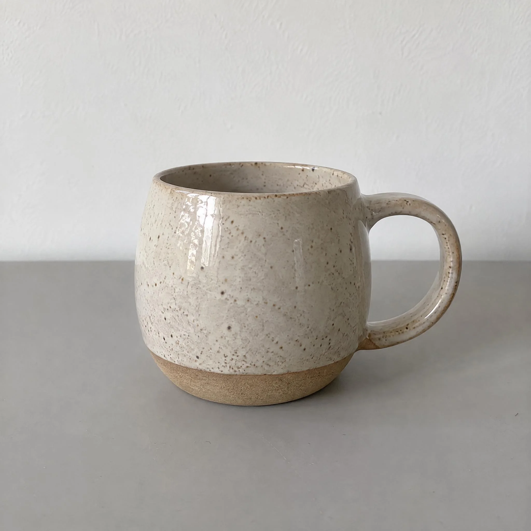 Speckled stoneware mug with an unglazed sandy base on a light grey table