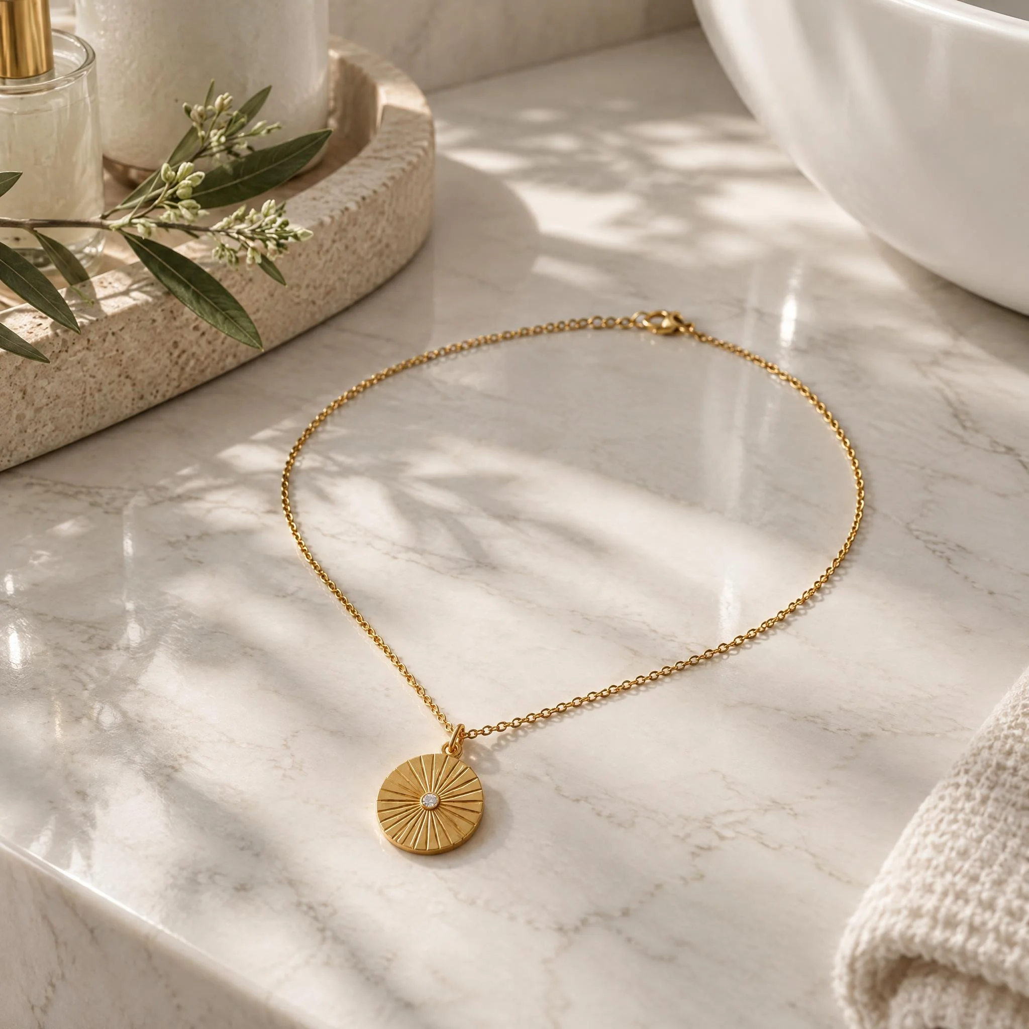 Gold medallion necklace lying on a marble bathroom counter in daylight